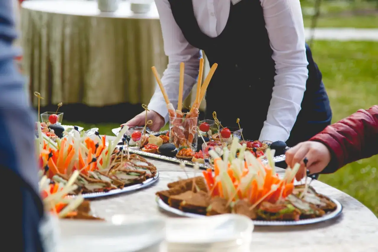 Camarero sirviendo canapés y sándwiches, mostrando varios tipos de servicios en restaurantes para un evento al aire libre.