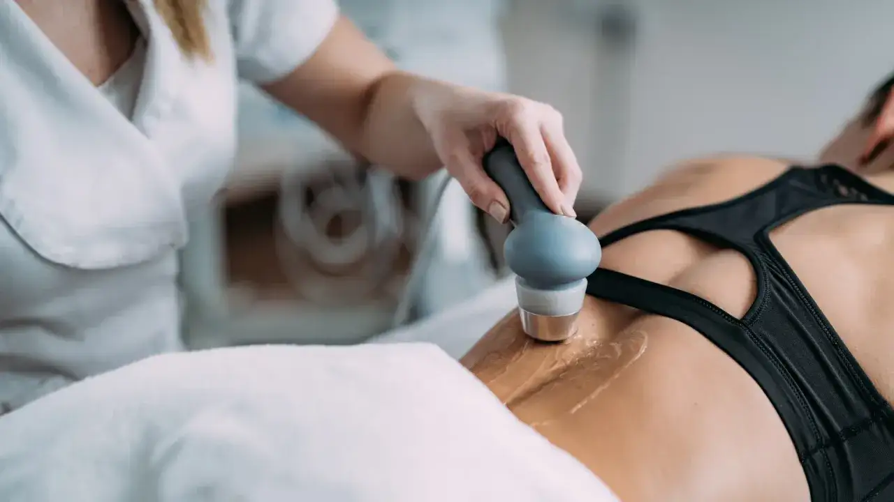 Fizjoterapeuta wykonuje zabieg ultradźwiękami na plecach pacjentki. Należy pamiętać o ultradźwięki przeciwwskazania.