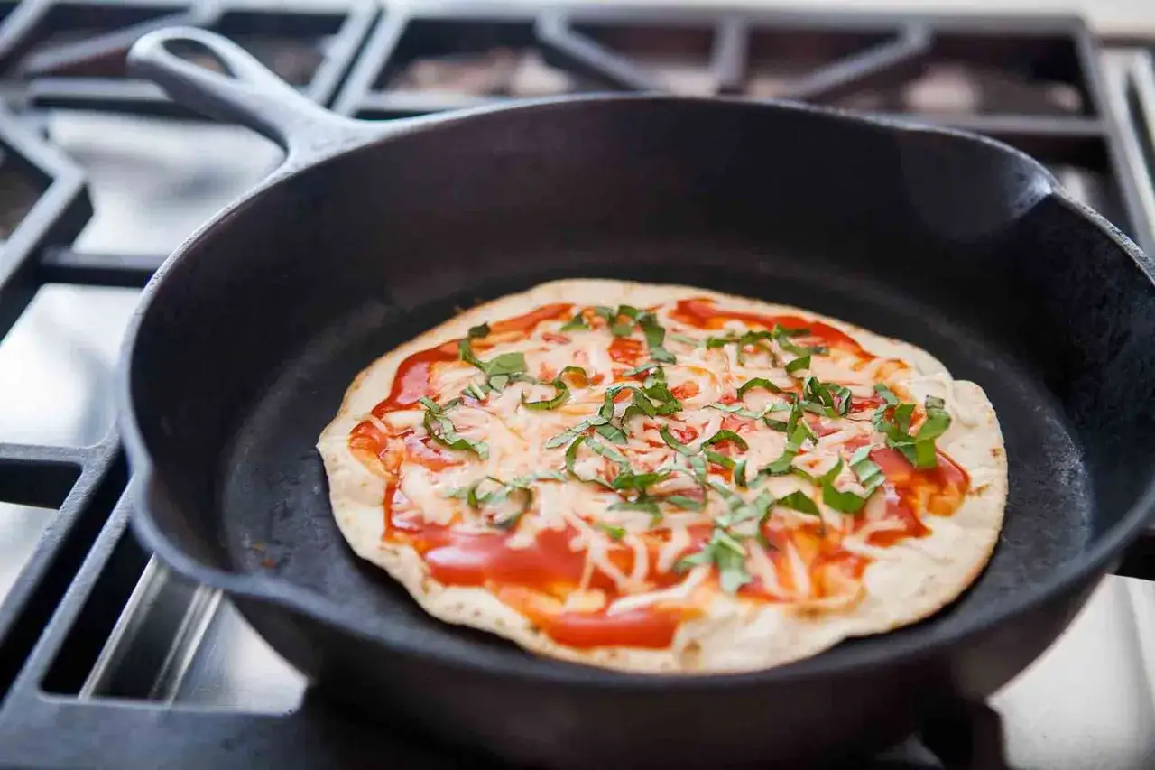 Szybka pizza z tortilli na patelni, z sosem, serem i bazylią, gotowa do podania.
