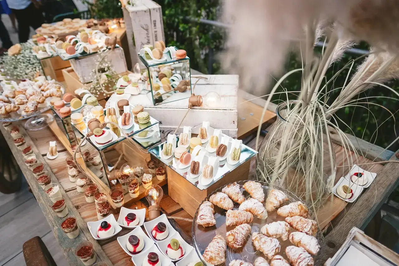 Dolce buffet per un aperitivo fuori chiesa matrimonio: macarons colorati, croissant e mini dessert su un tavolo rustico.