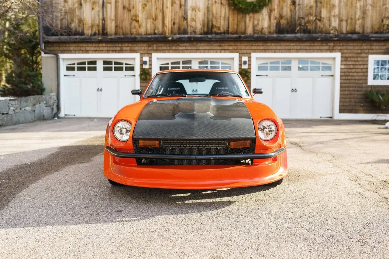 Pomarańczowy Datsun 280Z z karbonową maską przed garażem.