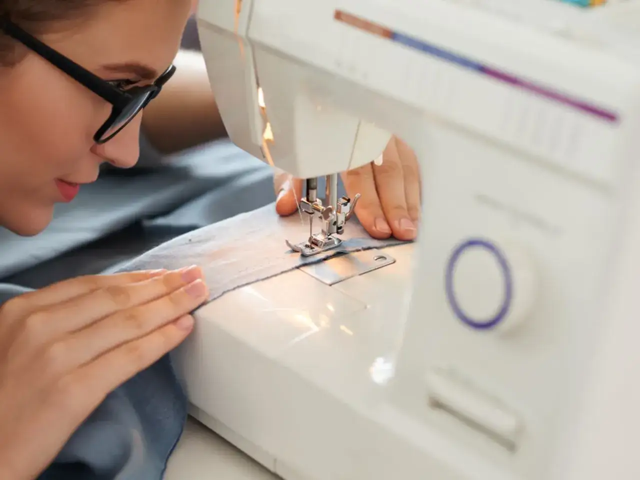Mujer concentrada con gafas trabajando en proyectos de costura con su máquina de coser.