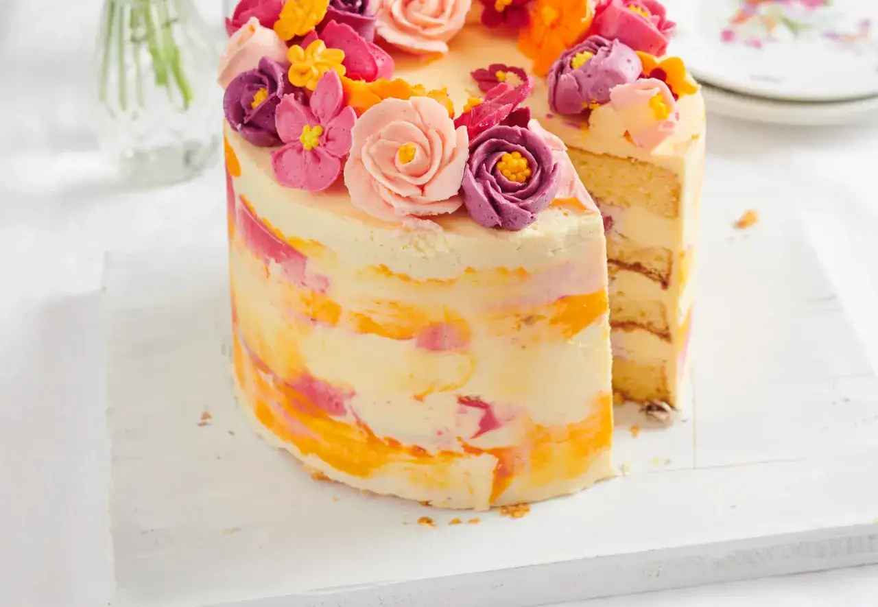 Bunter Kuchen mit amerikanischer Buttercreme-Blumen und Marmorierung. Ein St&uuml;ck ist herausgeschnitten.