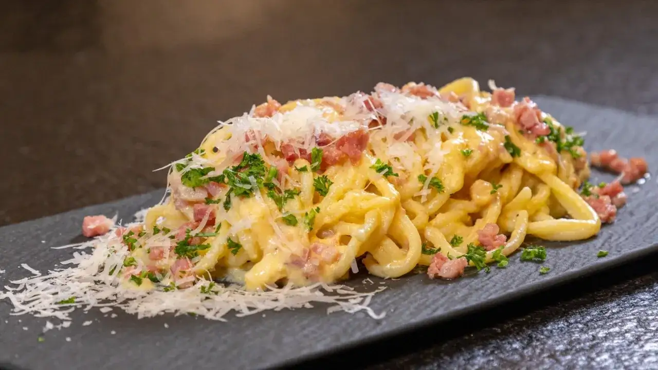 Ein Teller mit authentischer Spaghetti Carbonara, garniert mit Speckw&uuml;rfeln, frischer Petersilie und geriebenem Parmesan.