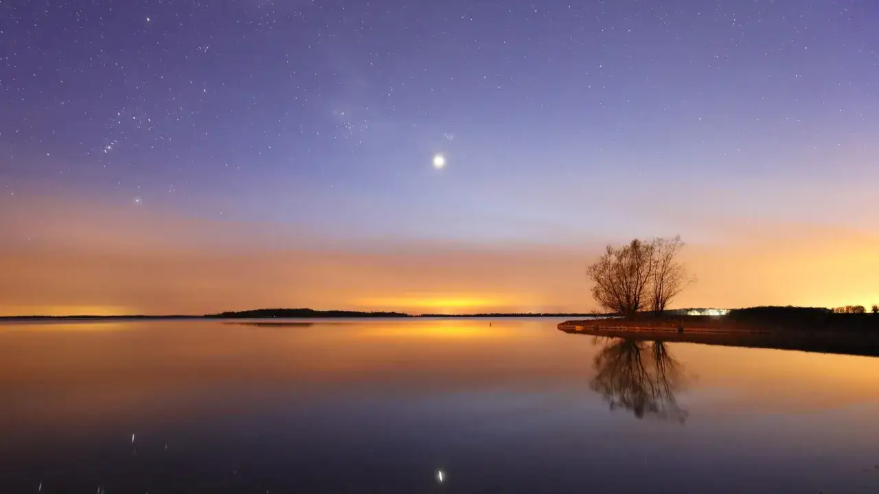 Spokojny wiecz&oacute;r nad jeziorem, gdzie odbija się pierwsza gwiazda na niebie.