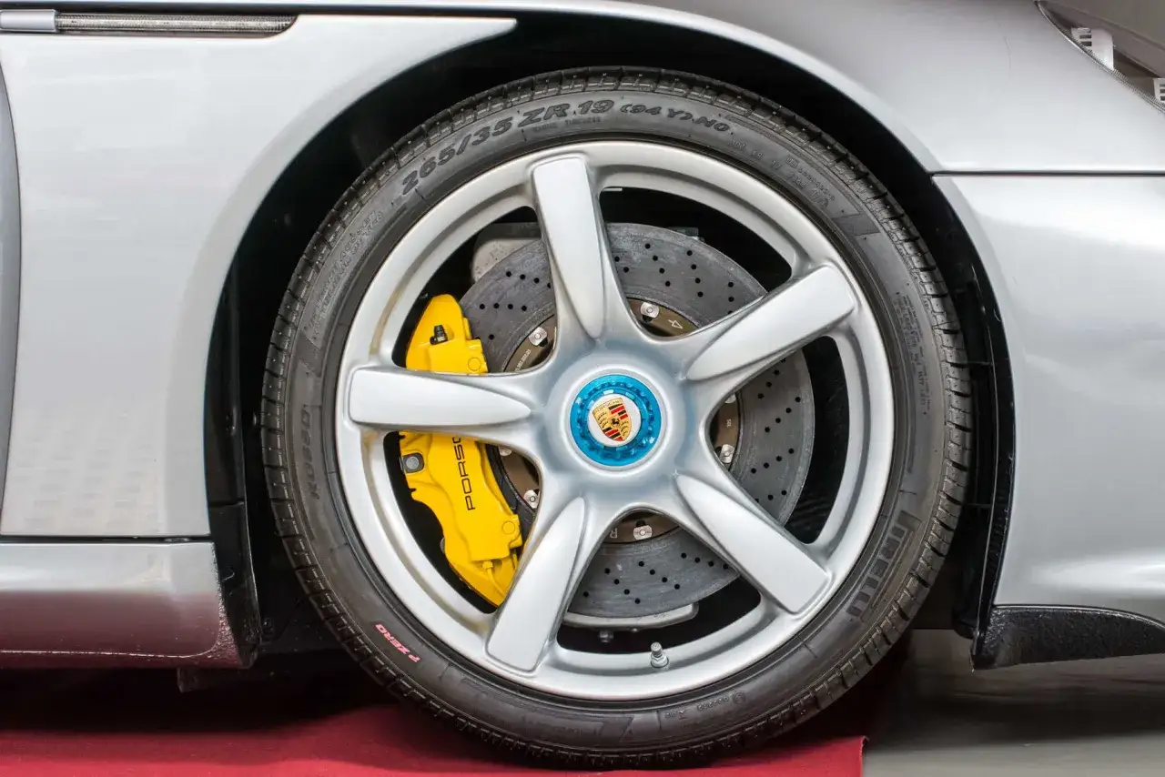 Nahaufnahme eines silbernen Porsche-Rads mit gelber Porsche-Bremse und gelochter Bremsscheibe.