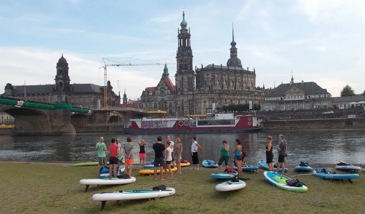 SUP-Fans am Elbufer in Dresden, bereit für eine Tour mit der Frauenkirche im Hintergrund.