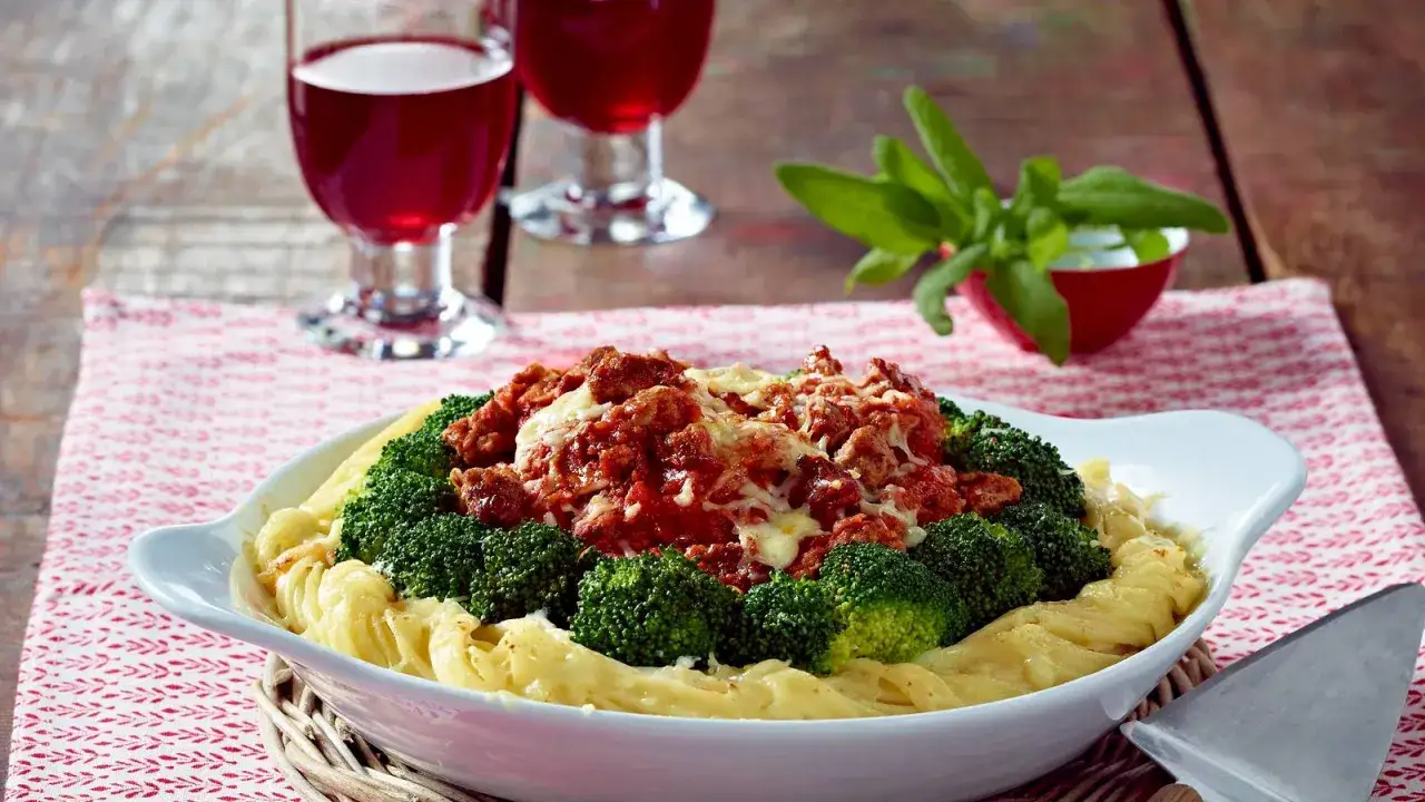 Herzhafte Brokkoli Bolognese mit geschmolzenem K&auml;se auf Bandnudeln, serviert mit Rotwein.