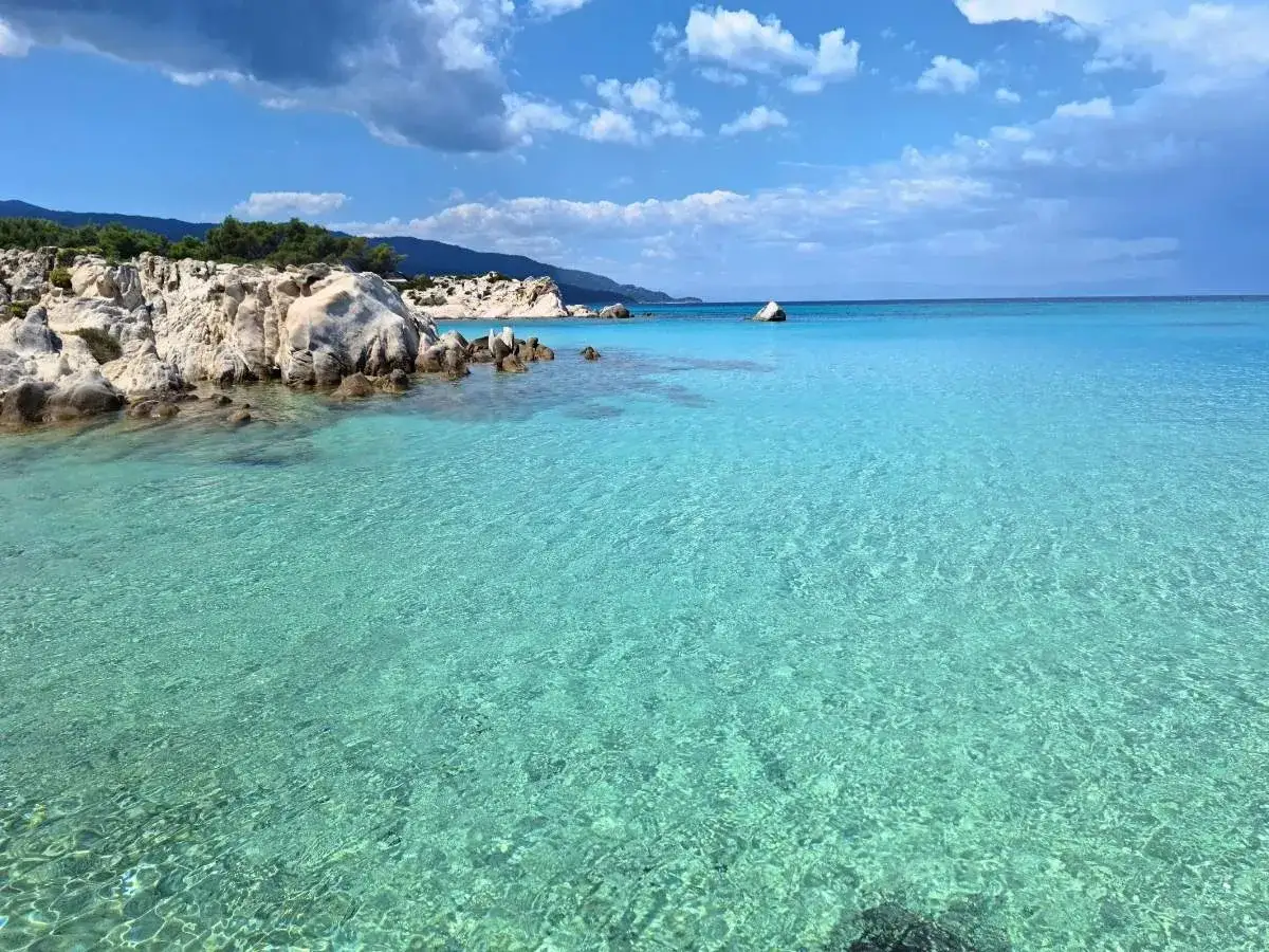 Turkusowe morze i skaliste wybrzeże na Chalkidiki. Słońce odbija się od wody, tworząc złociste refleksy na plaży.