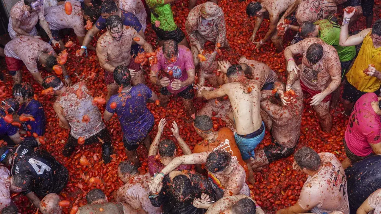 Multitud en la Tomatina de Buñol, España, lanzando tomates. La fiesta es un caos rojo y divertido.