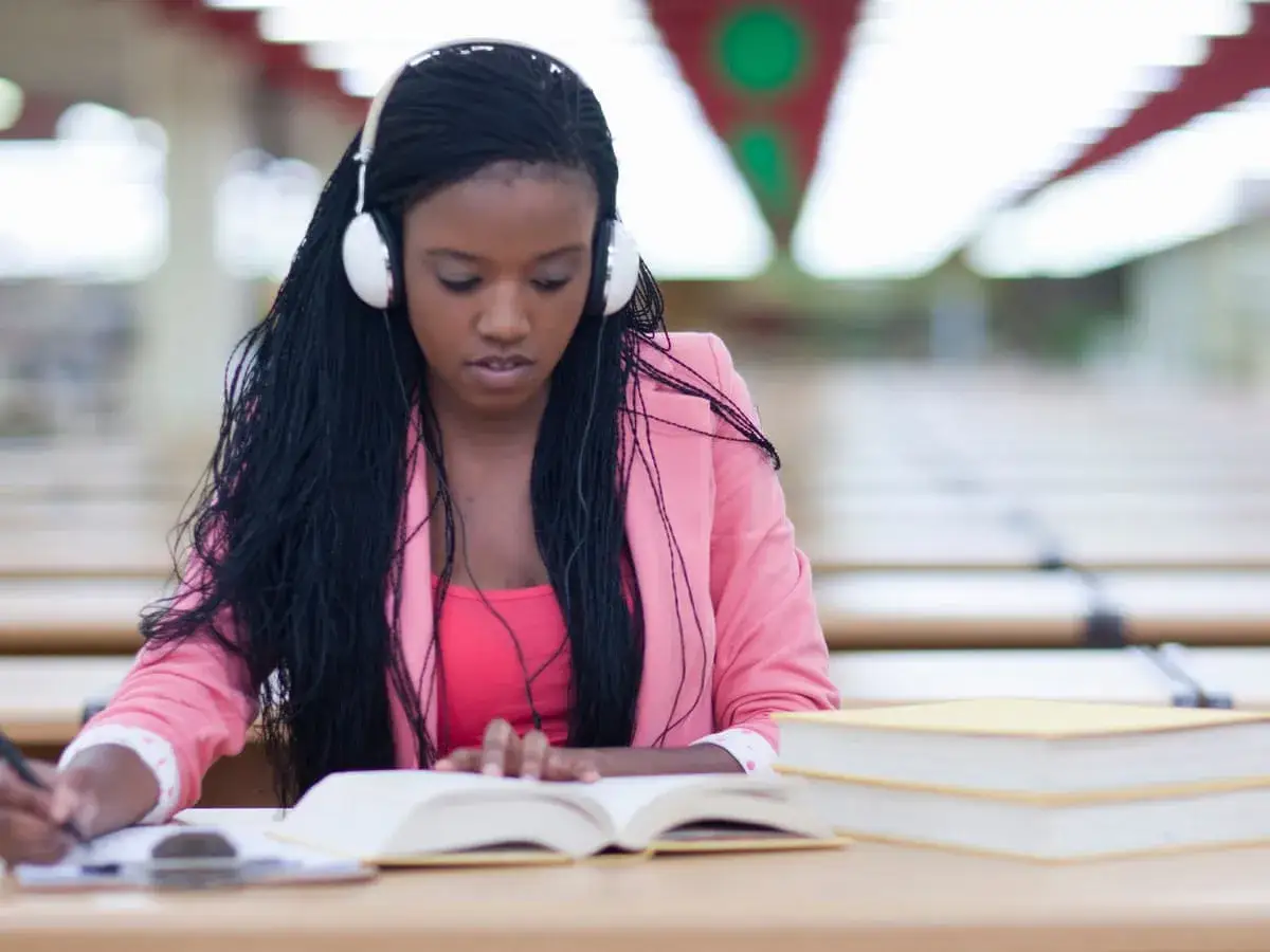 Junge Frau mit Kopfhörern lernt konzentriert mit Büchern. Musik beim Lernen hilft ihr, sich zu fokussieren.