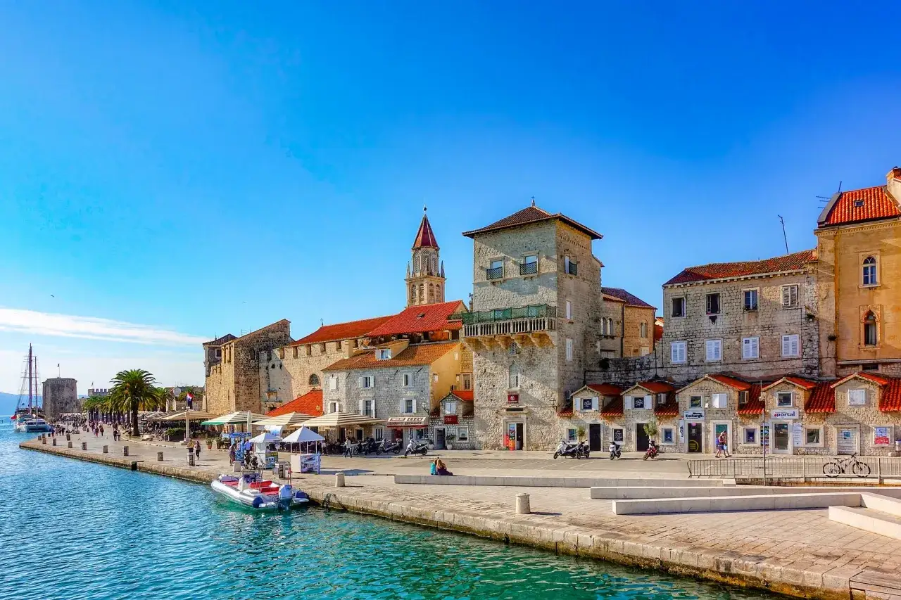 Trogir co zobaczyć: malowniczy deptak nad wodą, kamienne budynki, wieża kościelna i łodzie.