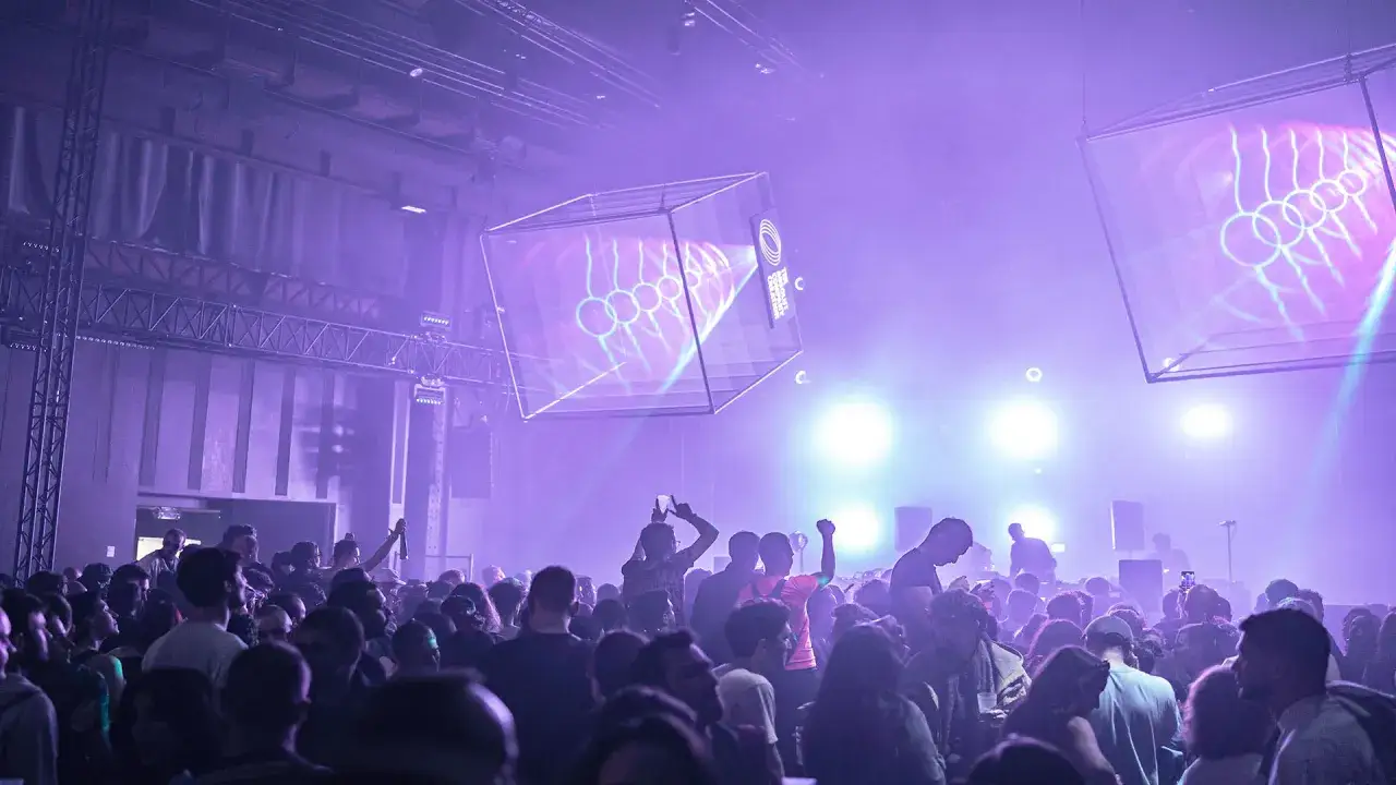 Foule en délire sous les lumières violettes, devant un écran projetant des formes abstraites. Un dj français anime la soirée.