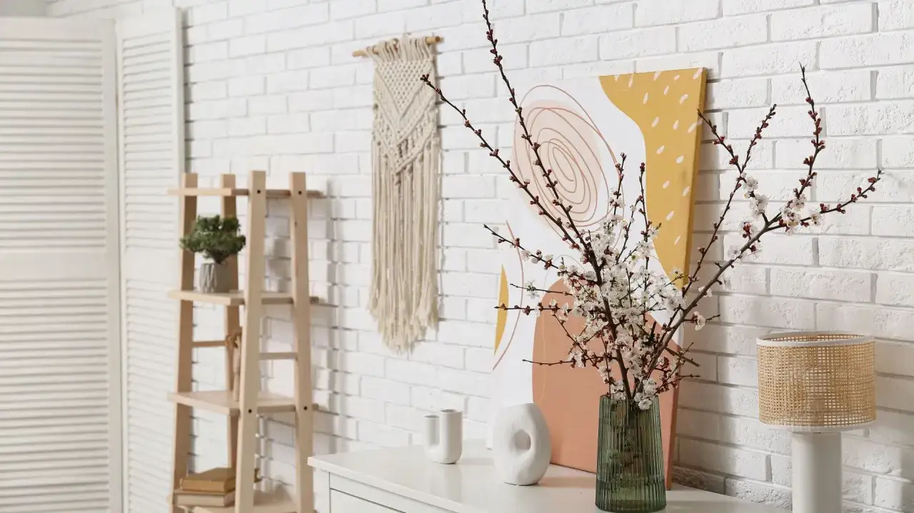 Zielony, prążkowany wazon z gałązkami kwitnącej wiśni. Obok stoi biała, ceramiczna ozdoba.
