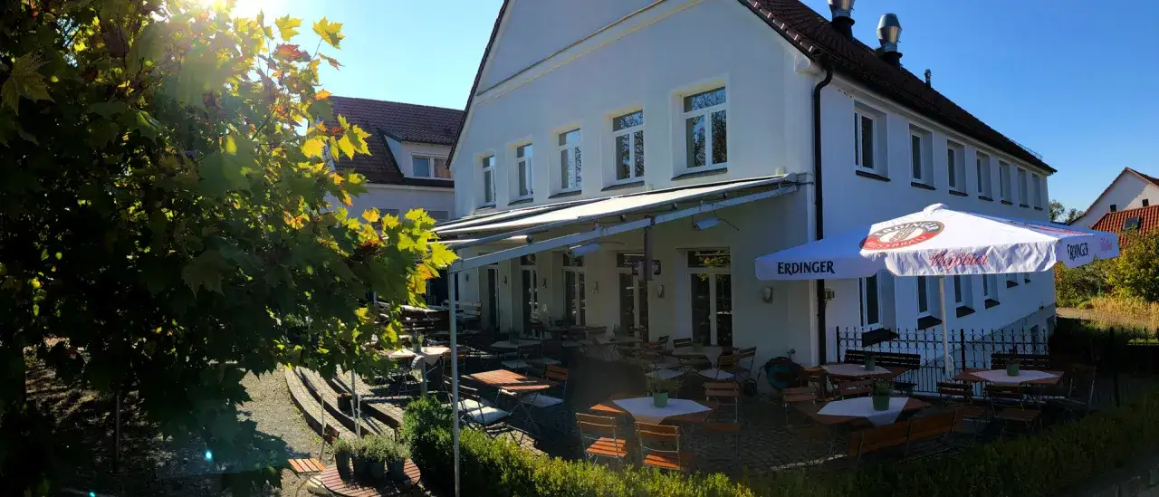 Einladende Biergarten-Atmosph&auml;re mit Tischen und St&uuml;hlen unter einem Sonnenschirm. Hier kann man in **hanffs ruh** die Sonne genie&szlig;en.