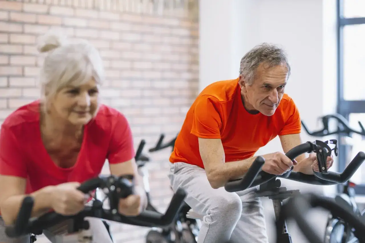 Un couple actif fait du v&eacute;lo d'appartement, prouvant qu'il n'est jamais trop tard pour rester en forme, m&ecirc;me fractionn&eacute; apr&egrave;s 60 ans.