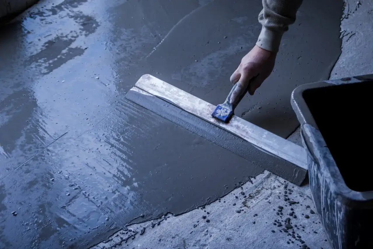 Main d'un ouvrier &eacute;talant du mortier pour un ragr&eacute;age ext&eacute;rieur de terrasse avec une taloche.