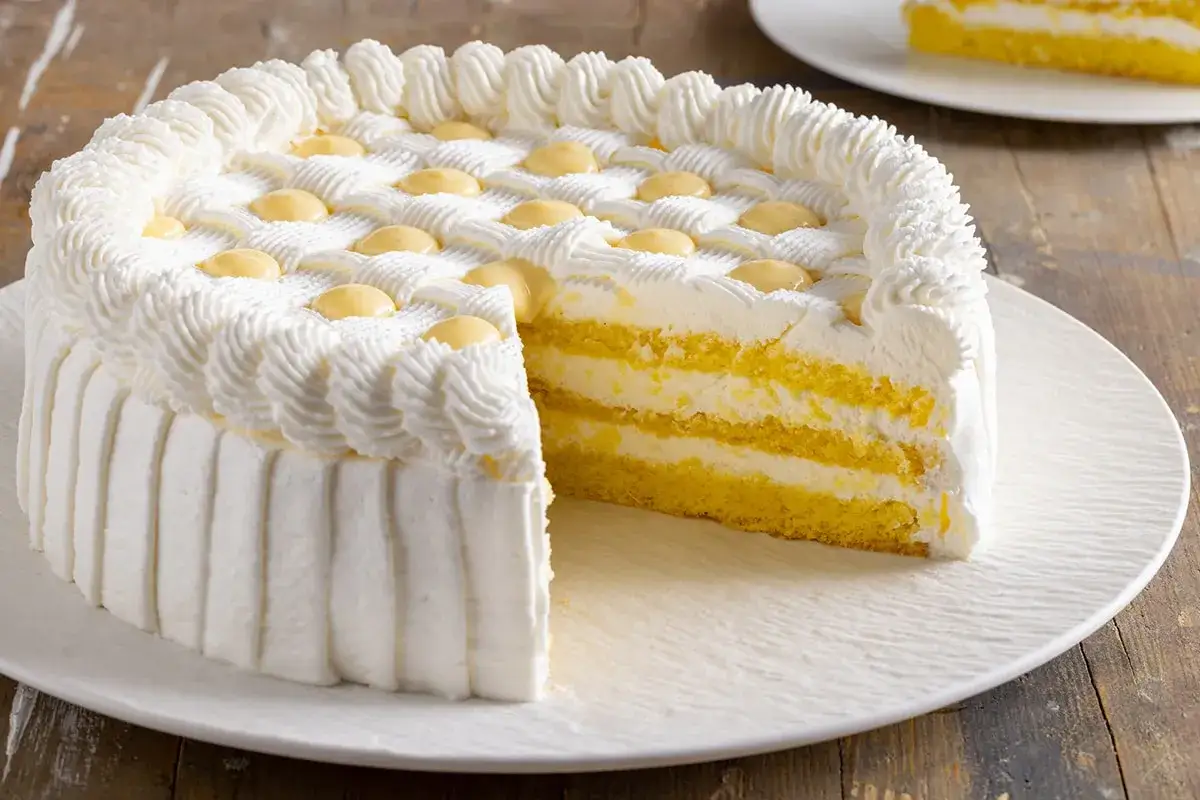 Torta compleanno invernale con pan di Spagna giallo, crema bianca e decorazioni a ciuffetti. Perfetta per festeggiare in ogni stagione.