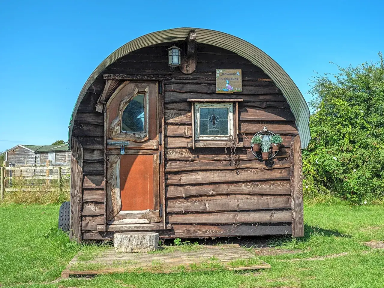 Uroczy, drewniany cottage z zaokrąglonym dachem, przypominający przytulną chatkę na kółkach.
