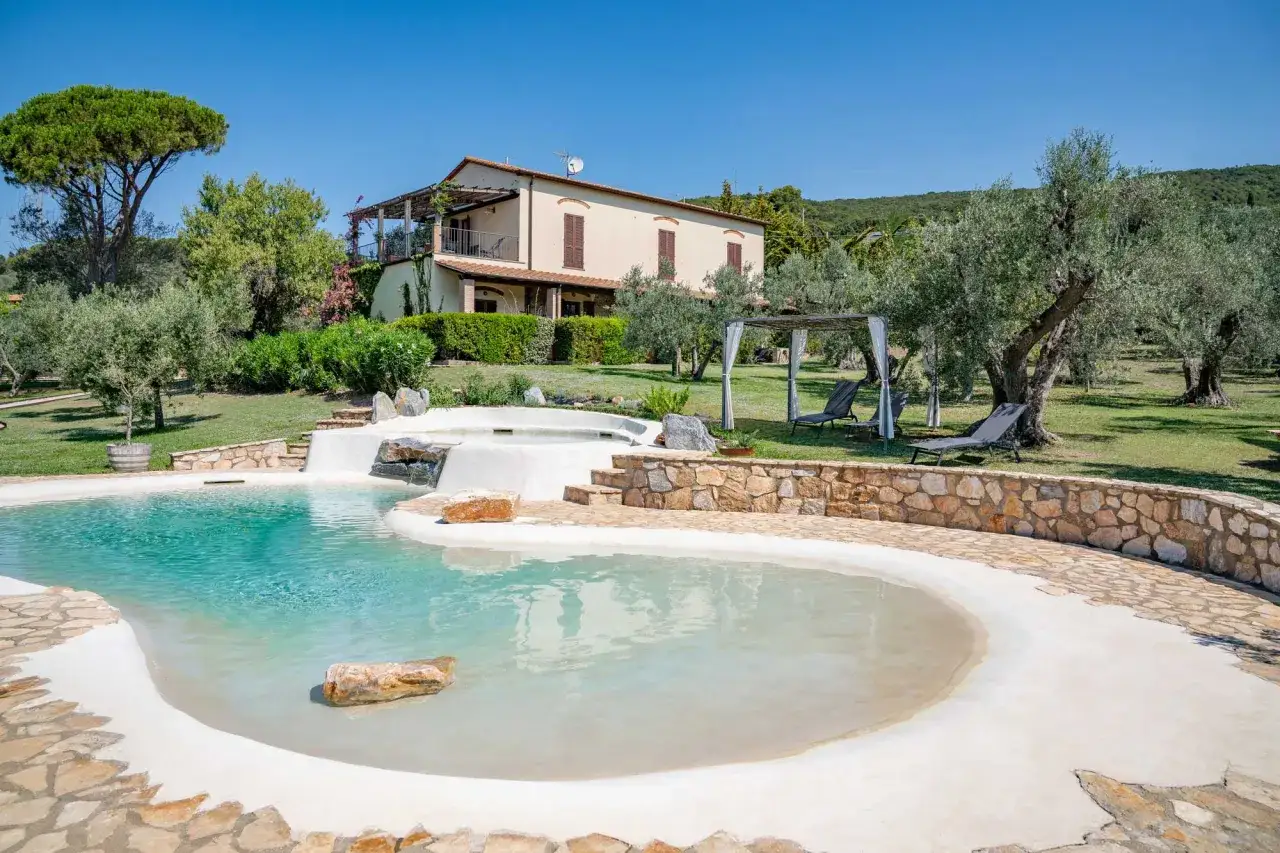 Piscina scenografica con cascata, ideale per un tour della Maremma. Villa toscana circondata da ulivi secolari e un prato verde.