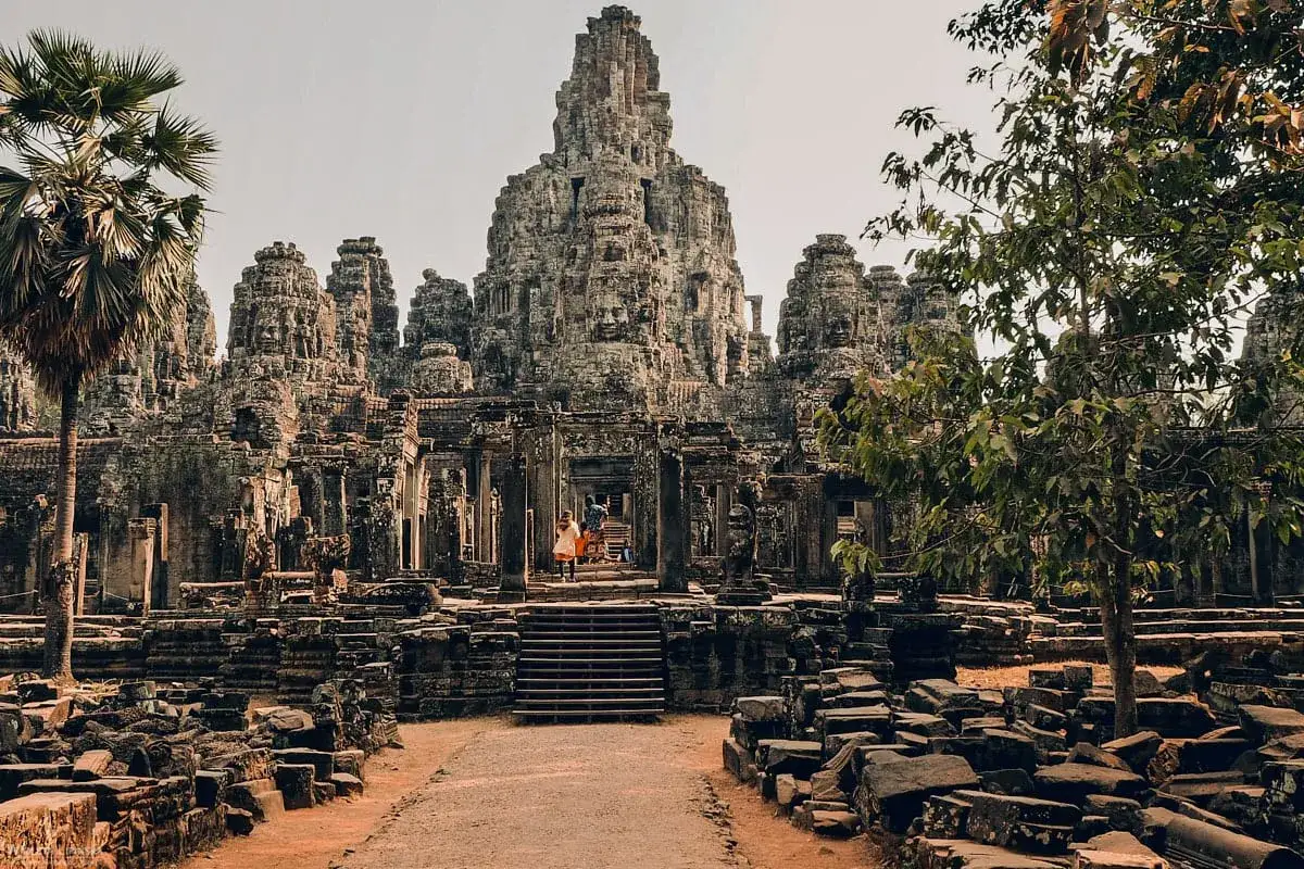 Kamienne twarze świątyni Bayon w Siem Reap. Dwie osoby wchodzą po schodach do starożytnego kompleksu.