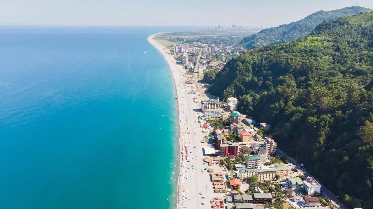 Widok z lotu ptaka na wybrzeże Gruzji. Turkusowe morze, piaszczysta plaża pełna ludzi i zielone wzgórza tworzą malowniczy krajobraz.