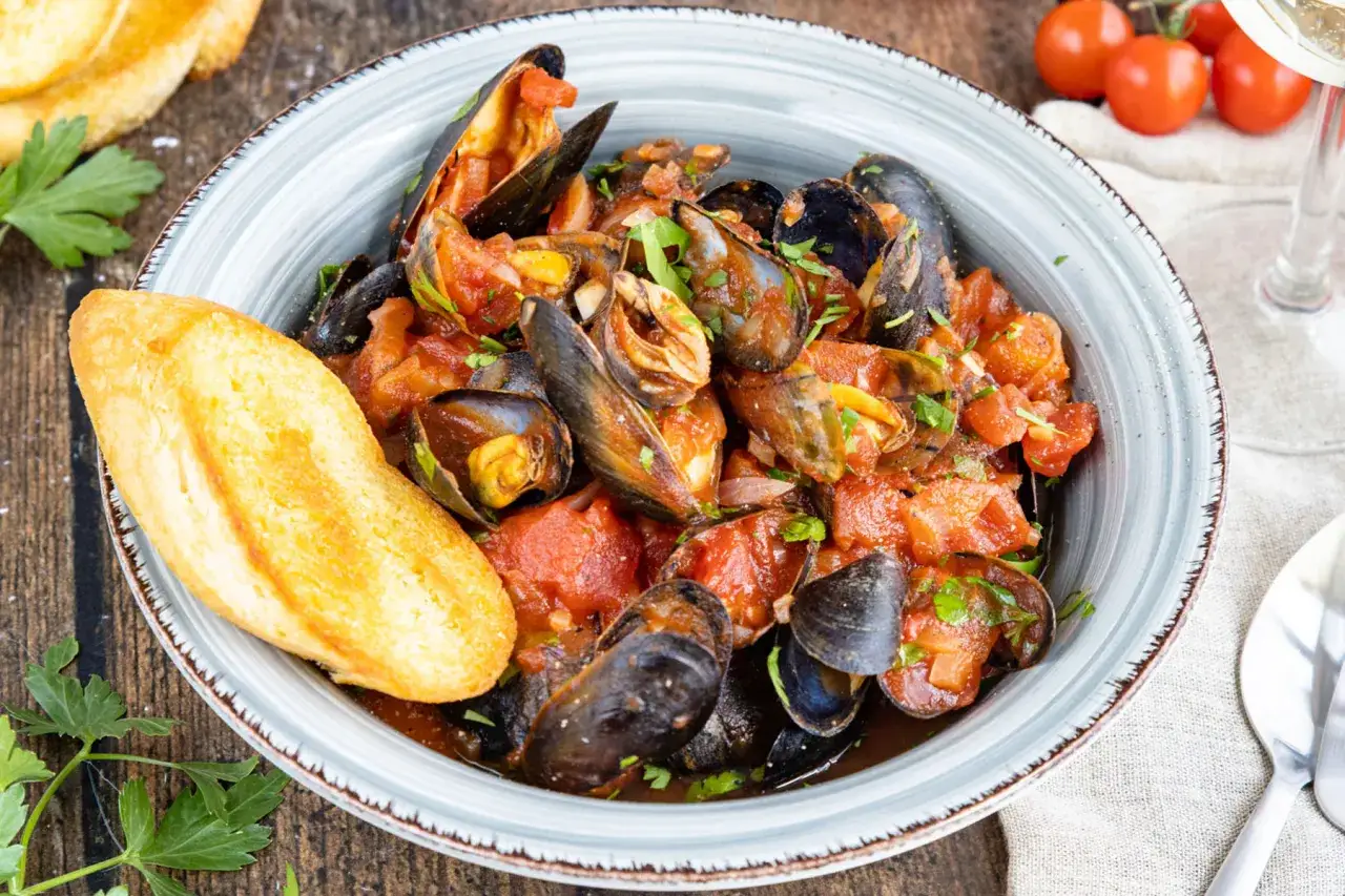 Schmackhafte Muscheln in Tomatensauce, garniert mit Petersilie und serviert mit knusprigem Brot. Ein Genuss für alle Sinne!