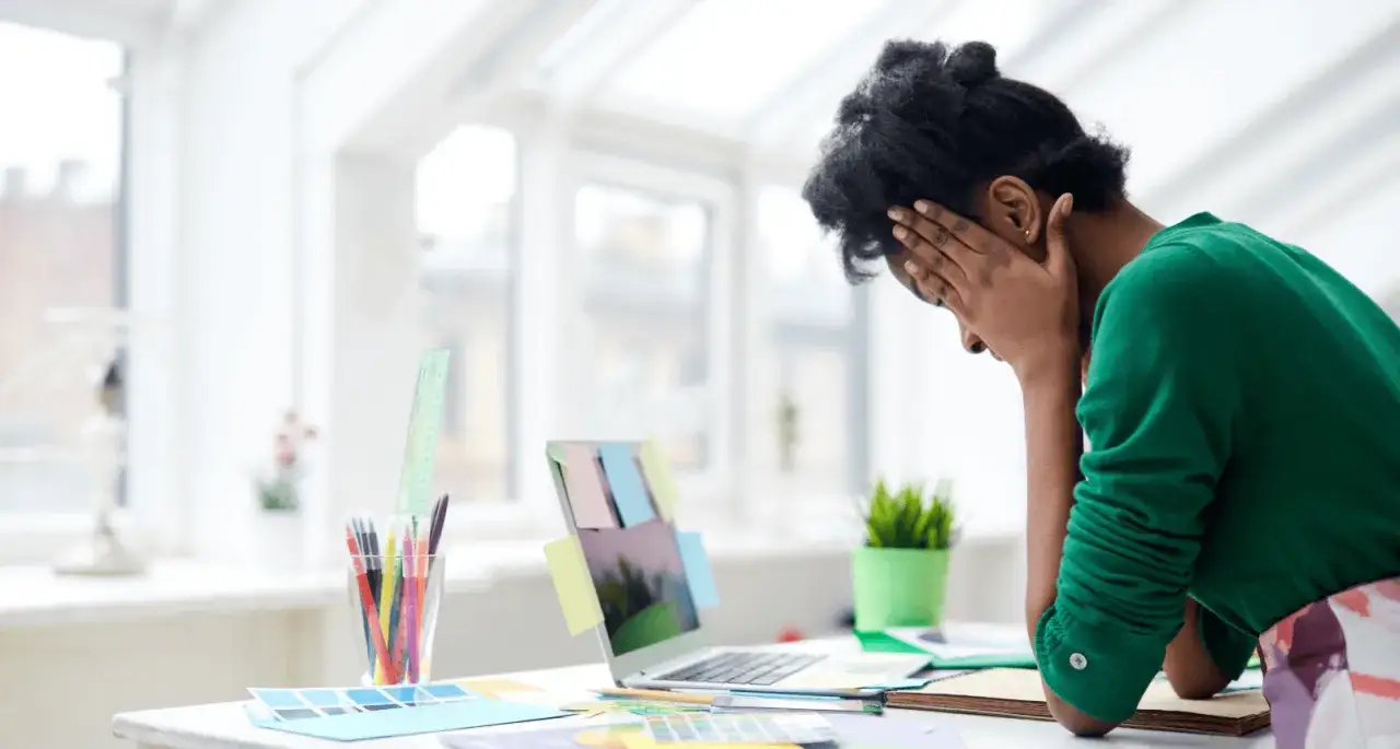Donna con le mani sul viso, frustrata dal lavoro. La mancanza di concentrazione causa stress e blocchi creativi.