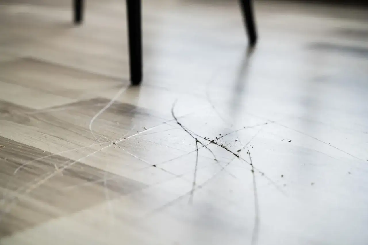 Zerkratzter Laminatboden unter einem Stuhlbein. Kratzer und Schmutz zeigen, dass es Zeit ist, Laminat reparieren.