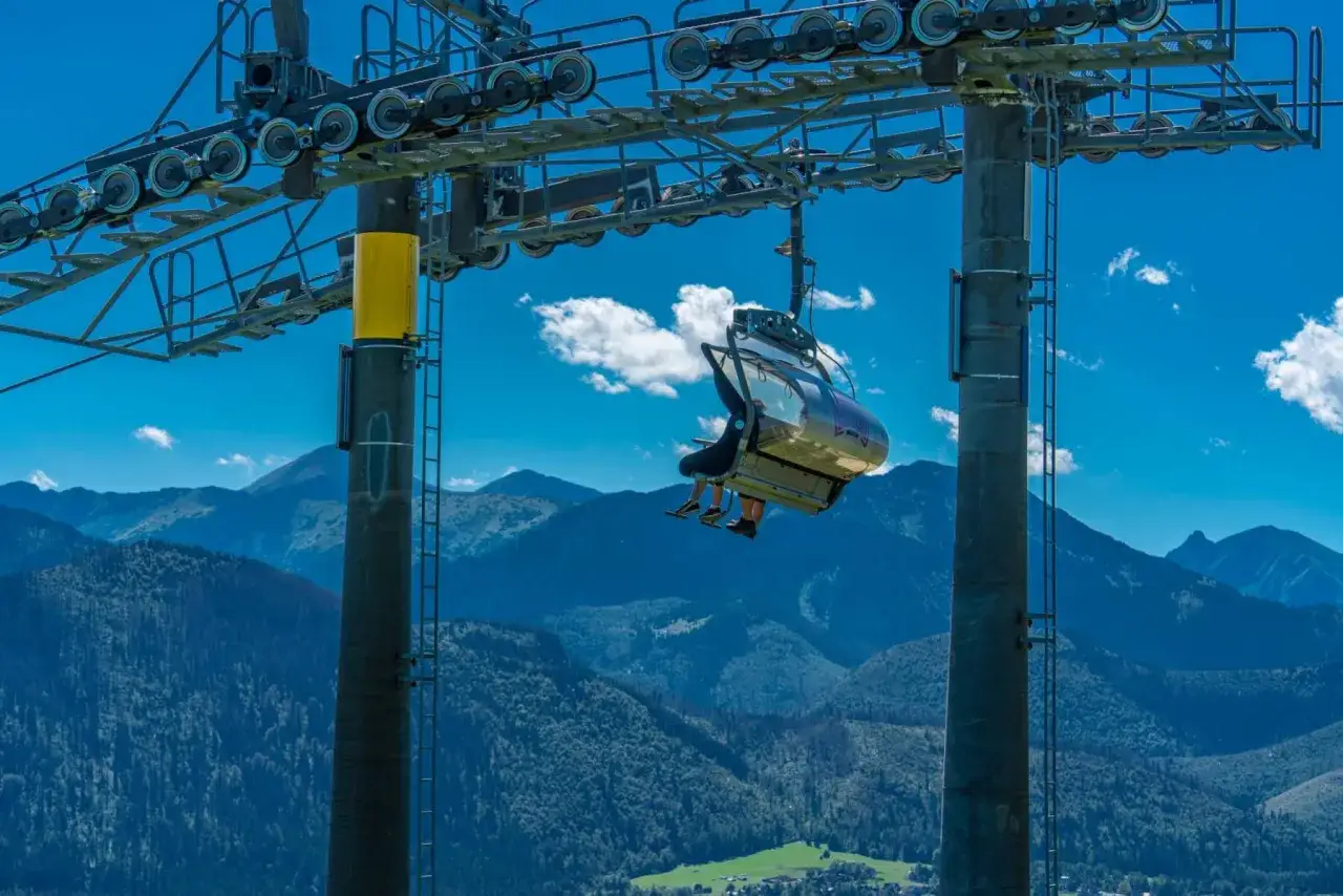 Wyciąg krzesełkowy Zakopane wwozi turyst&oacute;w na szczyt, skąd roztacza się widok na Tatry.