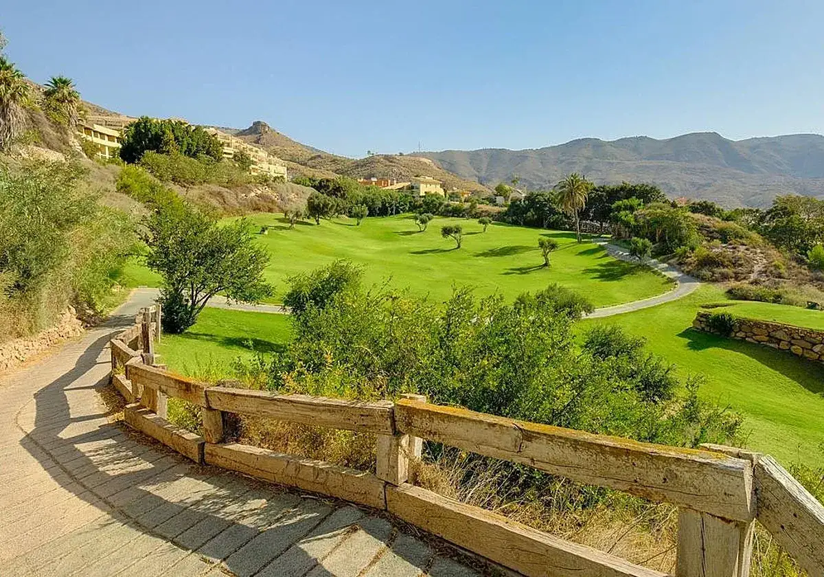 Un campo de golf verde y exuberante se extiende bajo el sol, con edificios residenciales en las laderas de la **sierra de Almer&iacute;a**.