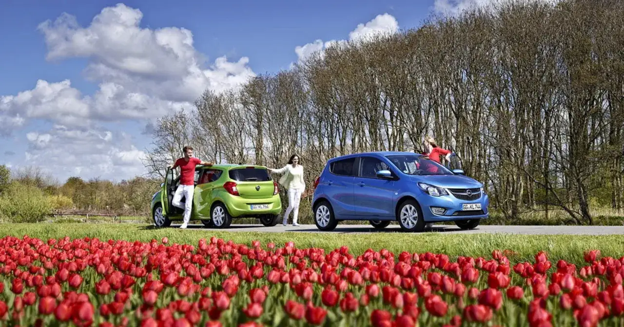 Zielony i niebieski Opel, najmniejszy Opel, na tle kwitnących tulipan&oacute;w i drzew.