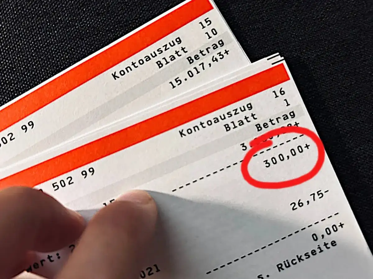 Kontoauszug zeigt eine Klimageld Auszahlung Deutschland von 300,00+. Ein Finger deutet auf den Betrag.