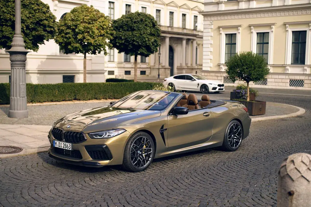 Ein goldfarbener BMW M8 Cabriolet steht auf Kopfsteinpflaster vor einem eleganten Gebäude.