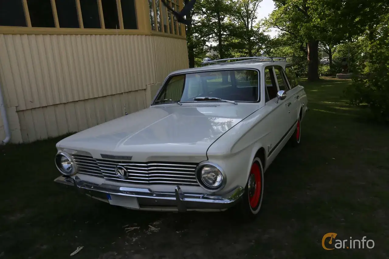 Vit Chrysler Valiant kombi parkerad vid en gul byggnad. Bilen har kromade detaljer och röda fälgar.