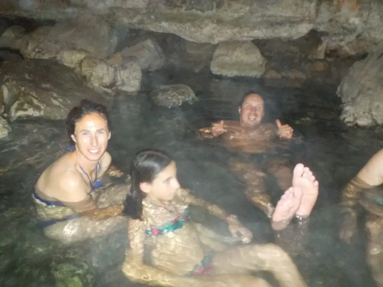Familia disfrutando de las pozas termales del r&iacute;o Deva, rodeados de rocas y agua c&aacute;lida.