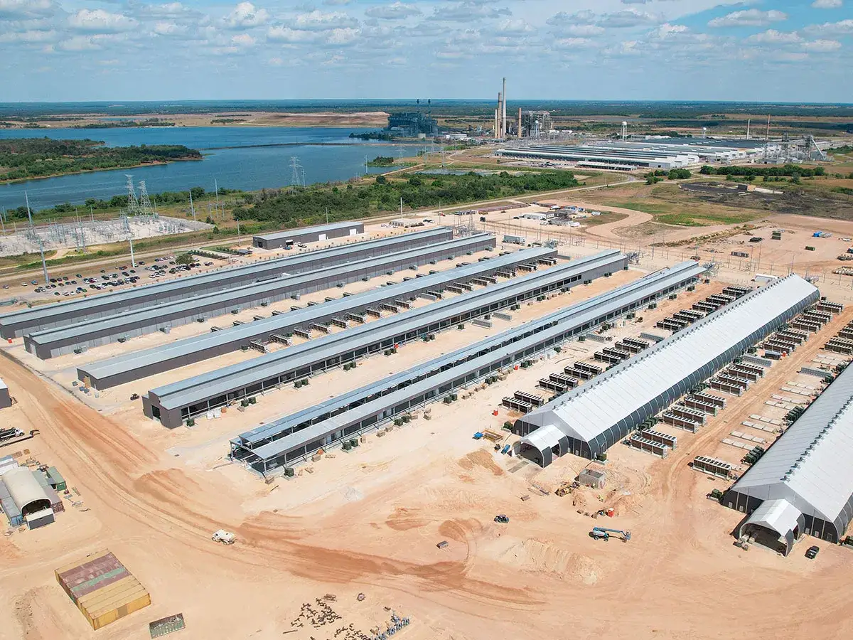 Gro&szlig;e Mining-Farm mit vielen Reihen von Server-Containern, die an ein Kraftwerk grenzen. Die Riot Platforms Aktie k&ouml;nnte von dieser Infrastruktur profitieren.