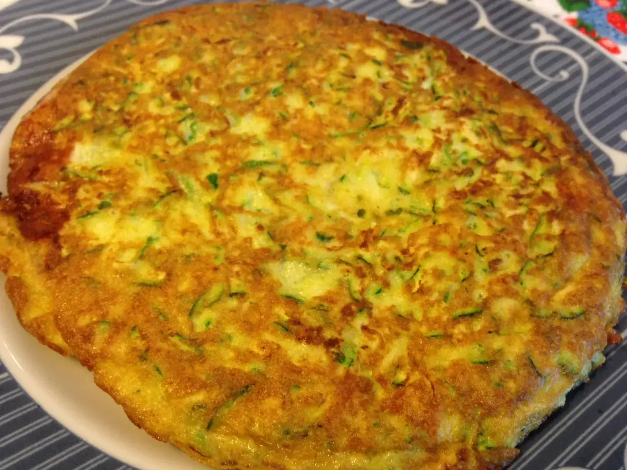 Frittata di zucchine in padella, dorata e invitante, con pezzetti verdi di zucchina ben visibili.