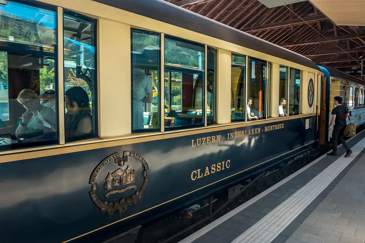 Der Zug von Luzern nach Genf, der GoldenPass Classic, h&auml;lt am Bahnsteig. Passagiere blicken aus den Fenstern.