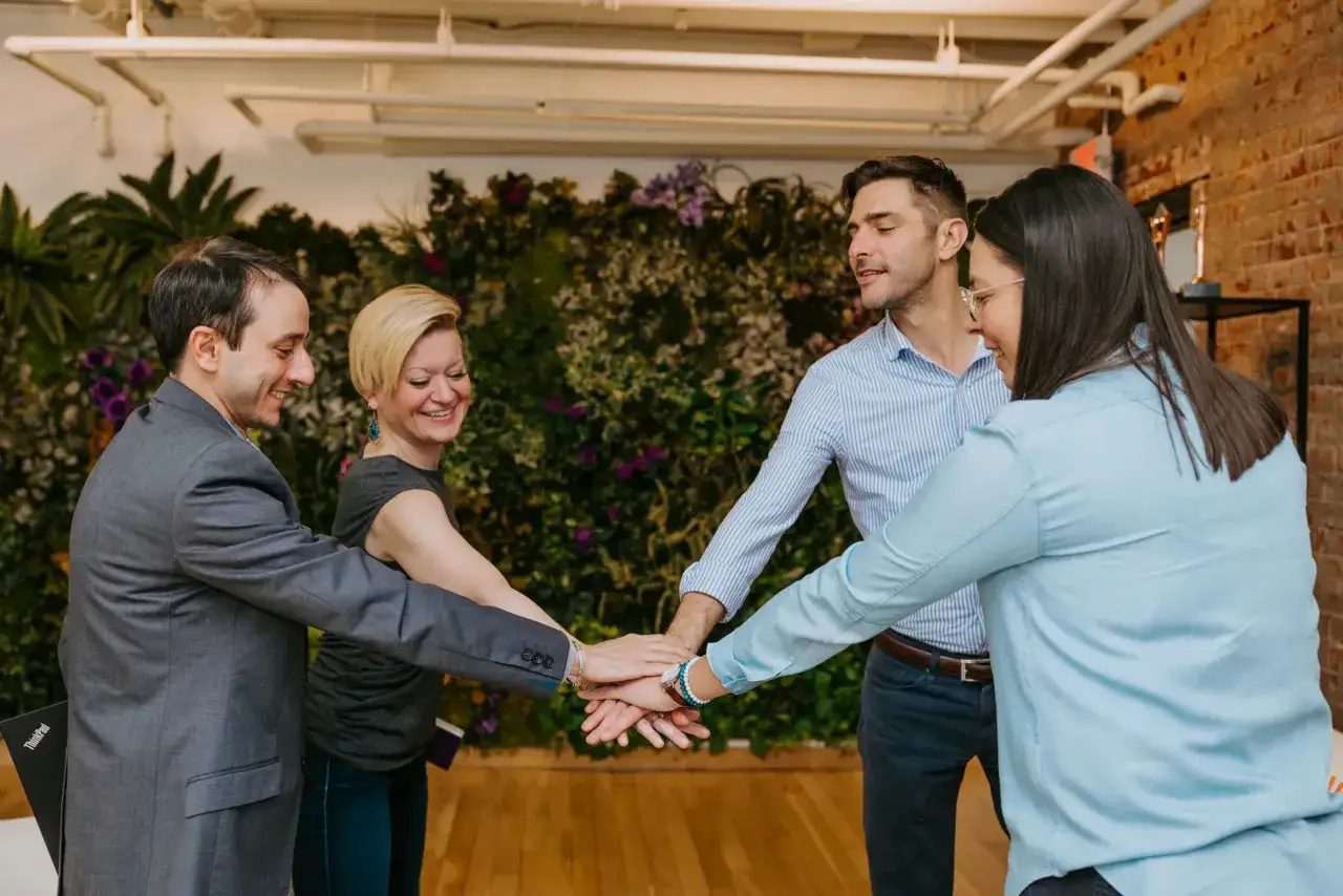 Four people with hands stacked in the center, smiling. This image represents teamwork and collaboration, key elements in effective coaching techniques for managers.