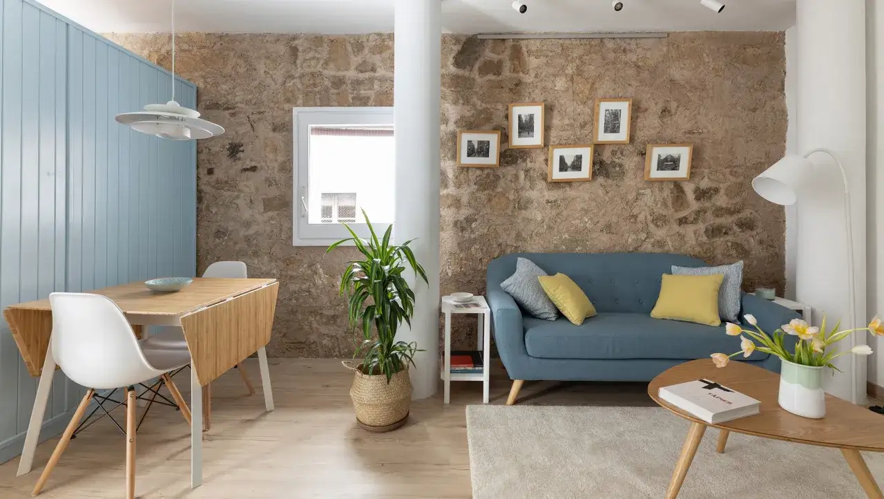 Un salón acogedor con paredes de piedra, un sofá azul y una mesa de comedor plegable. Un ejemplo de **tiny living** con estilo y funcionalidad.
