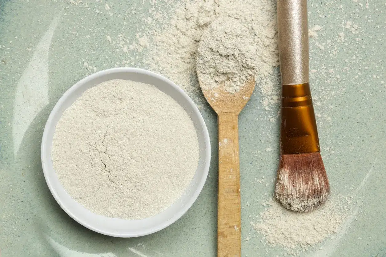 Biały proszek, czyli kaolin, w miseczce, na drewnianej łyżce i pędzlu do makijażu.