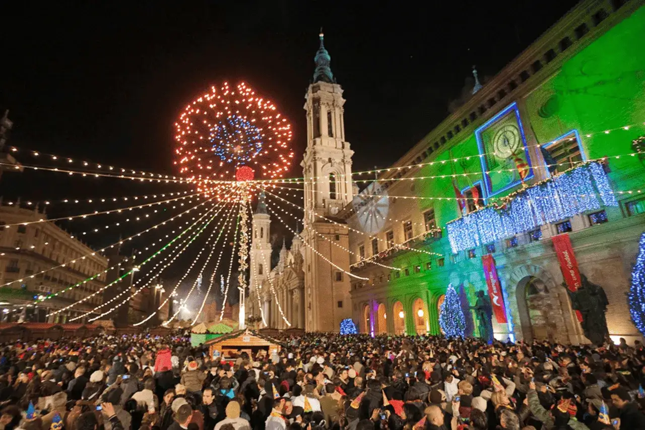 Multitud celebra la nochevieja Zaragoza con fuegos artificiales y luces festivas sobre la Basílica del Pilar.