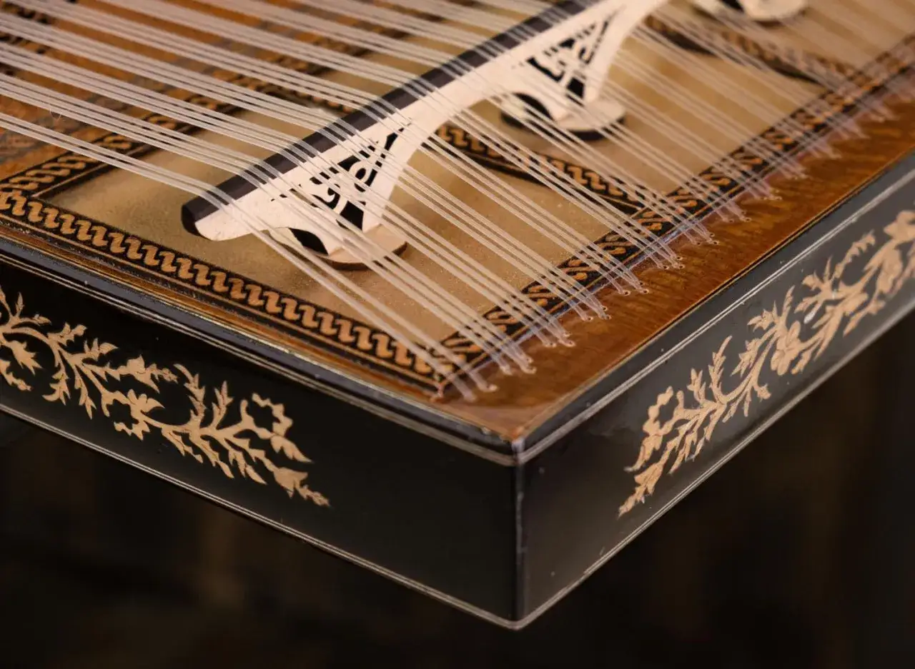 Un bel instrument &eacute;gyptien, un qanun aux cordes fines et &agrave; la caisse orn&eacute;e de motifs floraux dor&eacute;s sur fond noir.