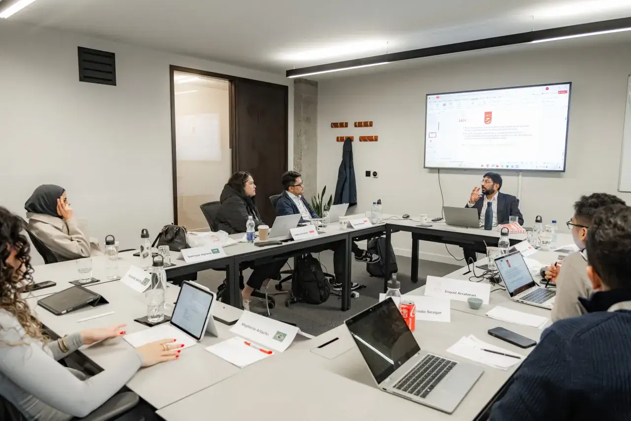 A diverse group discusses leadership coaching definition around a conference table, with laptops and notes.