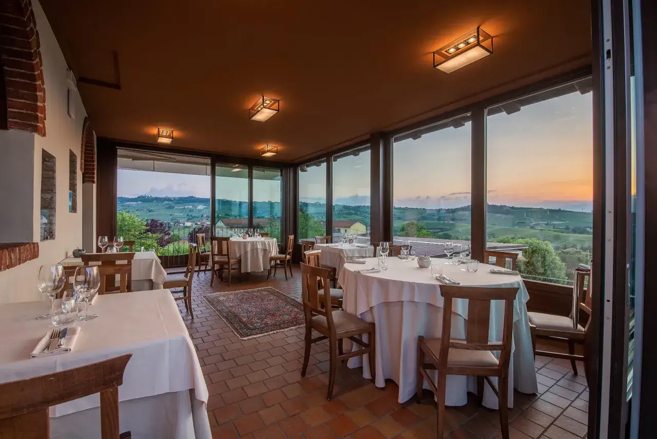 Tavoli apparecchiati in un ristorante con vista sulle colline delle Langhe al tramonto. Un luogo ideale per scoprire dove mangiare nelle Langhe spendendo poco, godendosi un panorama mozzafiato.