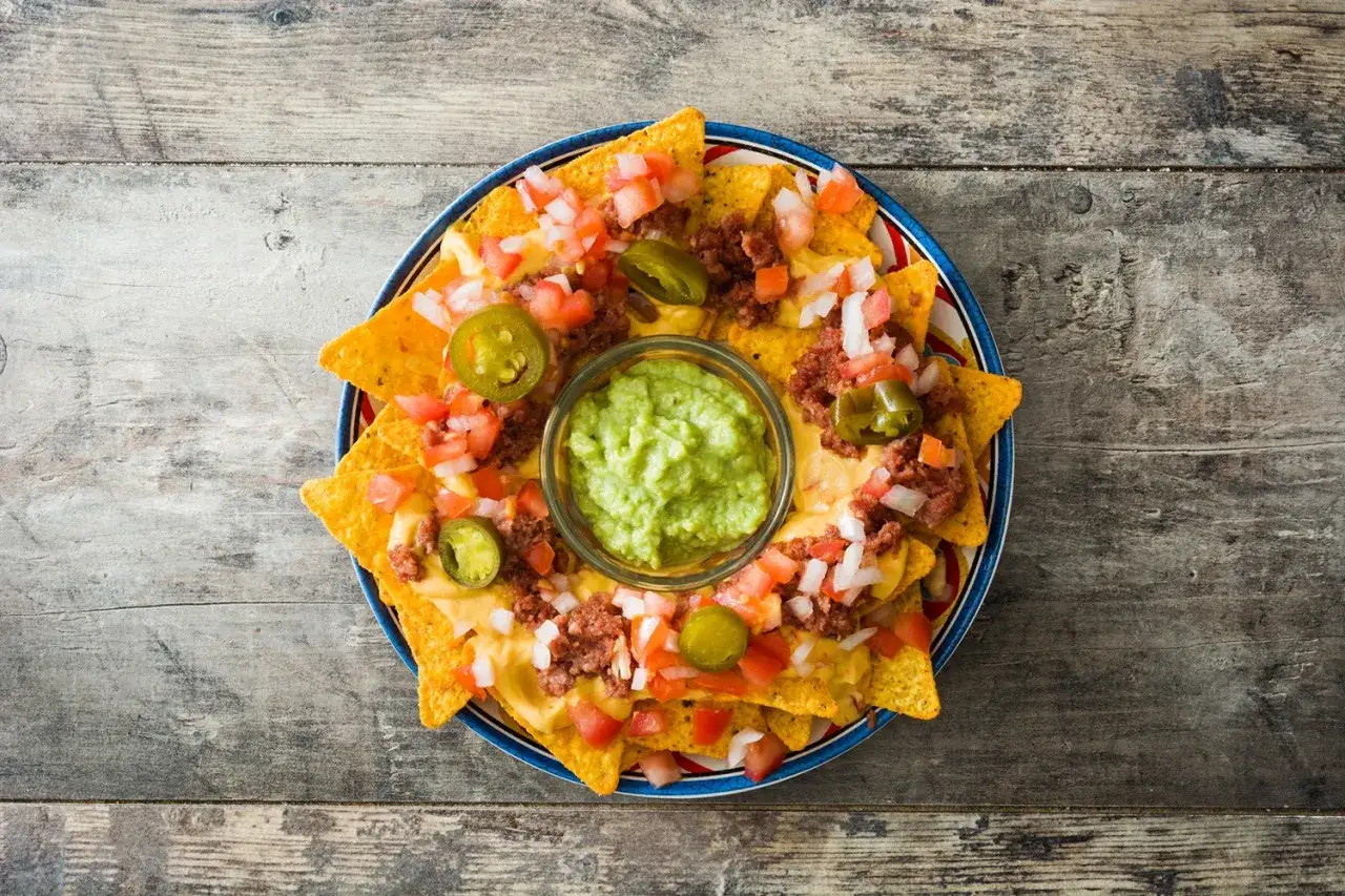 Nachos con guacamole y pico de gallo, cubiertos de queso derretido y jalape&ntilde;os. &iexcl;Un fest&iacute;n para compartir!