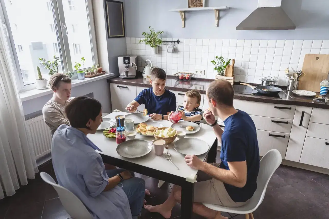 Familie beim Frühstück, um **Bindung aufzubauen**. Vater, Mutter und drei Kinder sitzen am Tisch, essen und unterhalten sich.