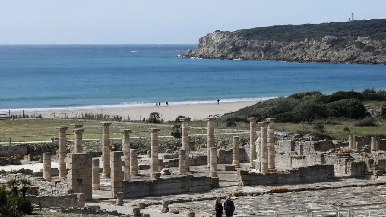 Ruinas romanas junto a la playa Baelo Claudia, con el mar azul y acantilados al fondo.