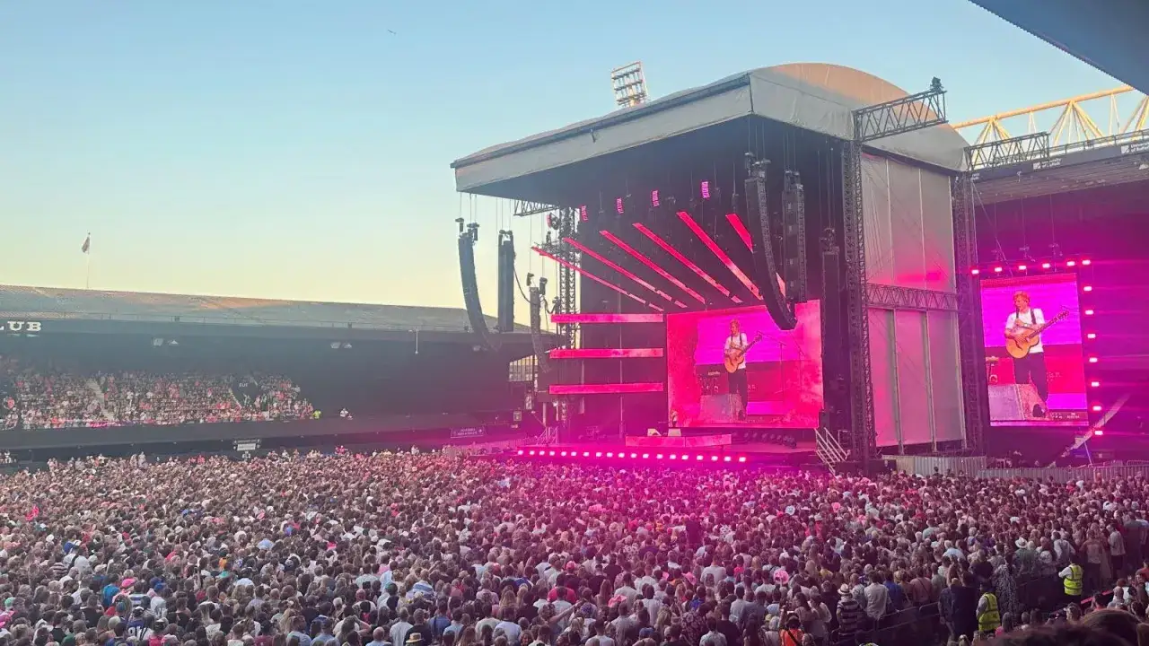 Ed Sheeran na żywo, tłum fan&oacute;w śpiewa jego przeboje. Koncert w stadium, r&oacute;żowe światła.
